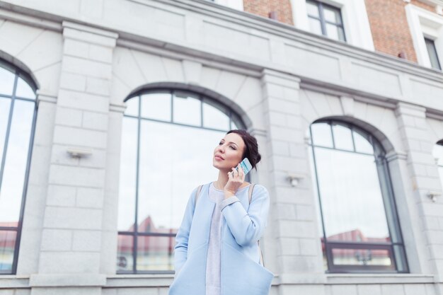 Atrakcyjna brunetka bizneswoman rozmawia przez telefon komórkowy z klientem na tle budynków biurowych