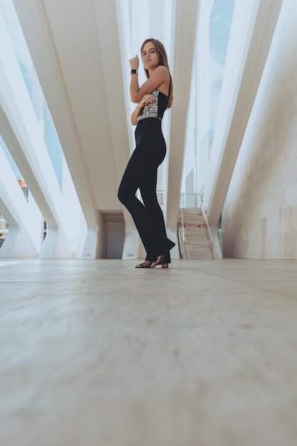 Atrakcyjna brunetka dziewczyna o idealnej figurze pozuje w holu budynku w czarnym stroju