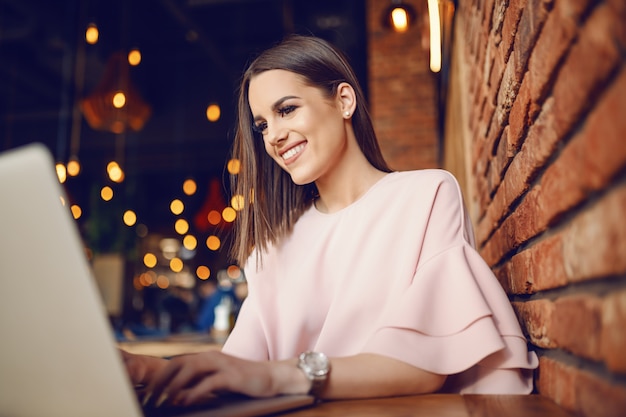 Atrakcyjna brunetka używa laptop podczas gdy siedzący w bufecie