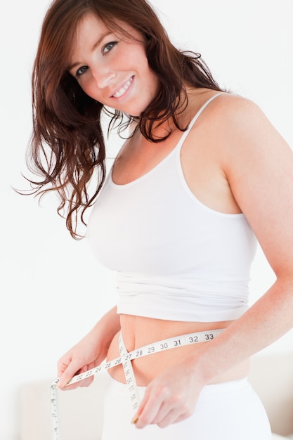 Atrakcyjna brunetki kobieta mierzy jej brzucha z taśmy miarą podczas gdy stojący