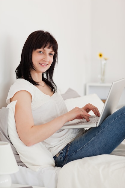 Atrakcyjna brunetki kobieta relaksuje z jej laptopem podczas gdy siedzący na łóżku