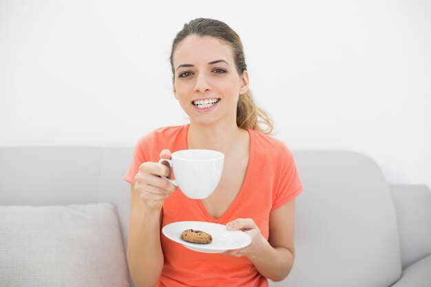 Atrakcyjna brunetki kobieta trzyma filiżankę ono uśmiecha się radośnie przy kamerą