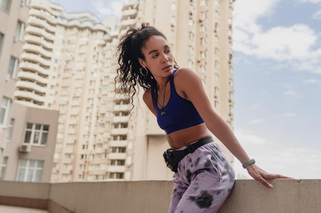 Atrakcyjna czarna afroamerykanka w sportowym stroju fitness na dachu wykonująca ćwiczenia