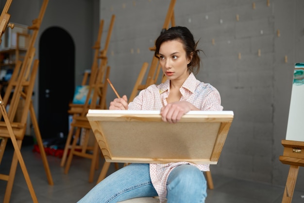 Atrakcyjna dorywcza młoda kobieta artystka trzymająca płótno w ręku rysując obraz farbami i pędzlem widok z przodu. Koncepcja ludzi, wypoczynku i hobby