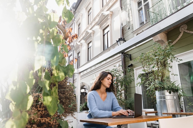 Atrakcyjna dziewczyna freelancer pracuje online na laptopie w kawiarni na świeżym powietrzu Pewna kobieta biznesu menedżer z laptopem pracuje z kolegami online w kawiarni