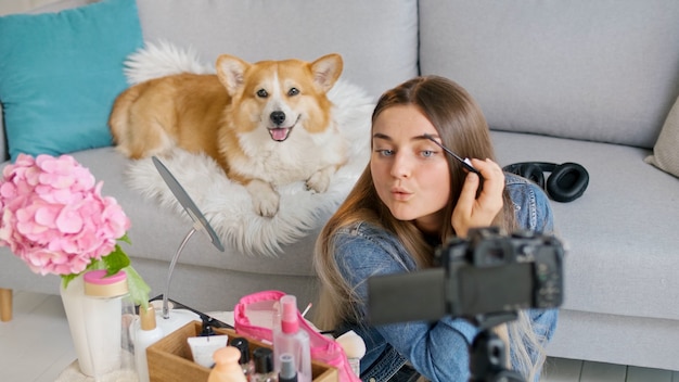 Atrakcyjna dziewczyna nastolatka z jej ładny pies vlogowania podczas dokonywania Makeup.Young Girl fotografowania jej wideoblog piękna. Młoda dziewczyna prowadzi zdalne nauczanie makijażu podczas blogowania.