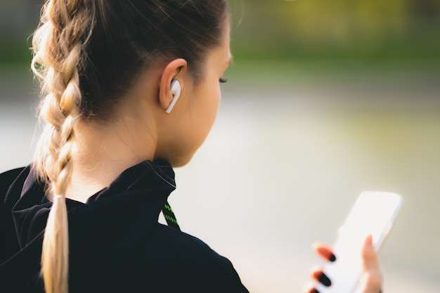 Zdjęcie atrakcyjna dziewczyna używa jej telefonu, bezprzewodowego hełmofonu podczas gdy biegający w parku