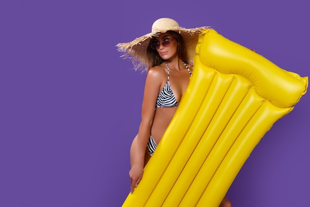 Atrakcyjna Dziewczyna W Bikini W Słomkowym Kapeluszu Trzyma żółty Materac Do Pływania Na Fioletowym Tle