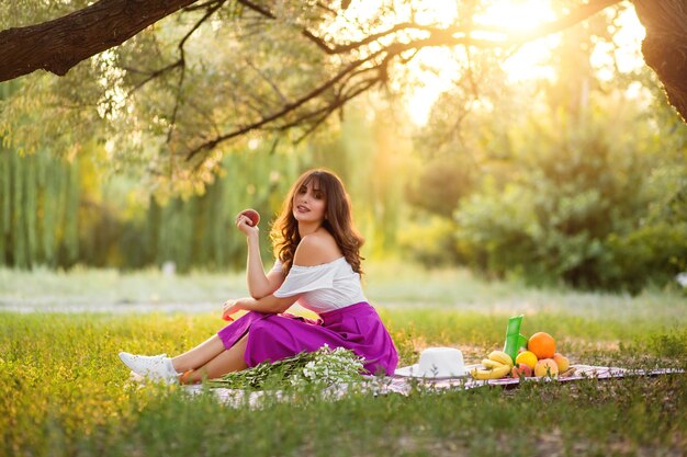 Atrakcyjna dziewczyna w sukience z odkrytymi ramionami na pikniku o zachodzie słońca