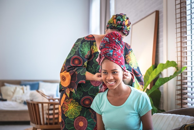 Zdjęcie atrakcyjna i młoda afroamerykańska kobieta ubiera się, zaczynając od nakrycia głowy, do którego pomogła jej siostra w afrykańskim koncepcie rodzinnym i narodowym.