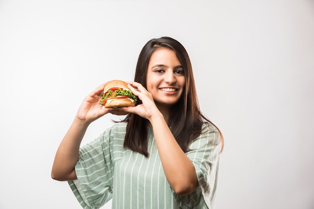 Atrakcyjna indyjska Azjatycka dziewczyna je burgera na białym lub żółtym tle