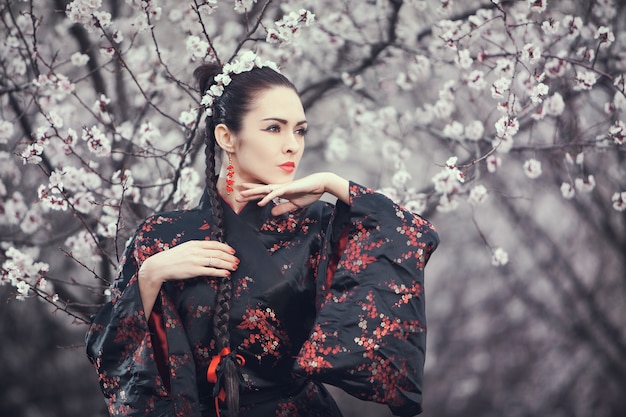 Atrakcyjna kobieta azjatyckich noszenie kimono stojący w kwitnącym ogrodzie.