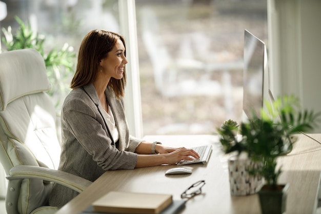 Atrakcyjna kobieta biznesu siedzi samotnie w swoim domowym biurze i pracuje na komputerze.
