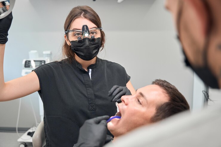 Atrakcyjna kobieta dentystka w dentystycznej lupie chirurgicznej dostosowuje lampę LED