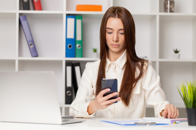 Atrakcyjna kobieta pracuje na inteligentny telefon w jej stacji roboczej.