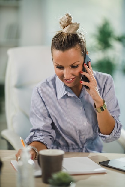 Zdjęcie atrakcyjna kobieta siedzi samotnie i rozmawia przez telefon komórkowy w ciągu dnia w domowym biurze.