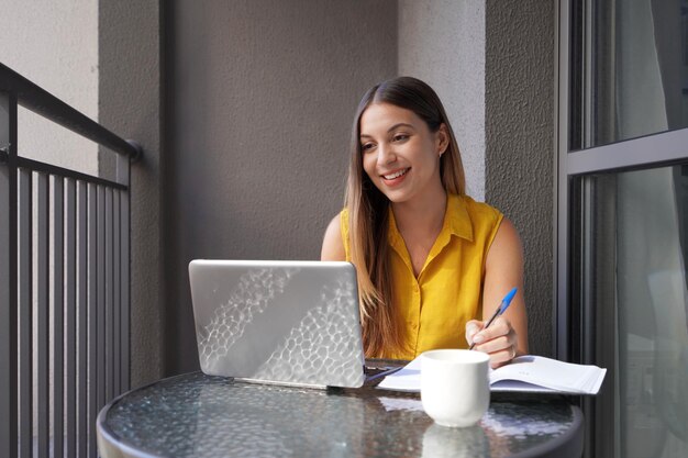 Atrakcyjna Kobieta Siedzi Z Laptopem Na Balkonie I Pracuje Patrząc Uważnie Na Ekran Piękna Dziewczyna Freelancer W Konferencji W Notebooku Siedzący Na Balkonu