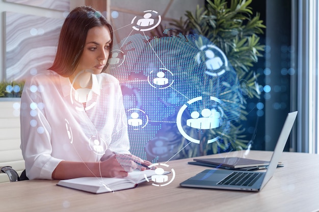 Atrakcyjna kobieta w białej koszuli w miejscu pracy pracy z laptopem, aby zatrudnić nowych pracowników dla międzynarodowego doradztwa biznesowego HR hologramowe ikony mediów społecznościowych na tle biura