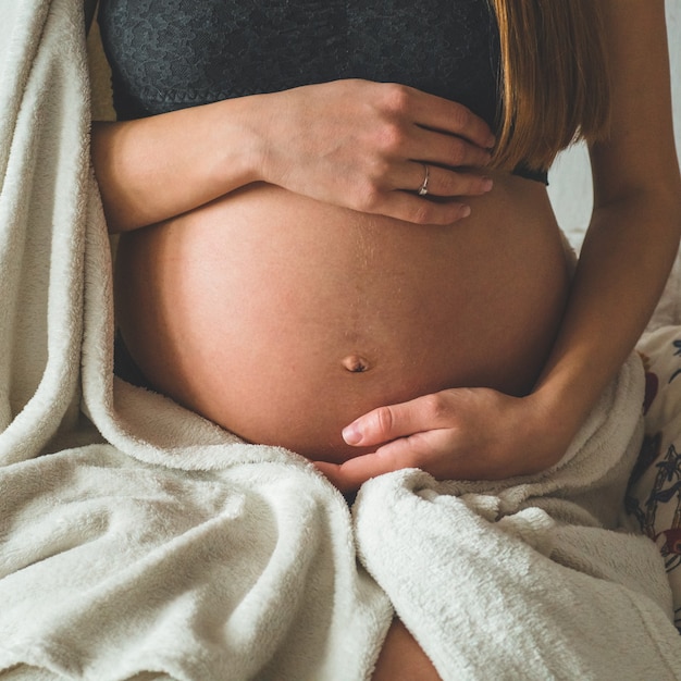 Atrakcyjna kobieta w ciąży siedzi na łóżku i trzyma jej brzuch. Ostatnie miesiące ciąży.