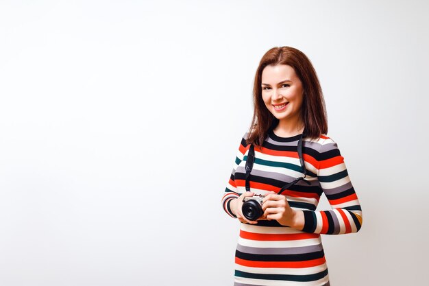 Atrakcyjna kobieta w kolorowej sukience trzyma aparat i uśmiecha się. Poziome studio strzał na białym tle. Skopiuj miejsce