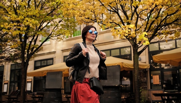 Atrakcyjna kobieta w okularach przeciwsłonecznych idzie ulicą z plecakiem promieniującym pewnością siebie i stylem