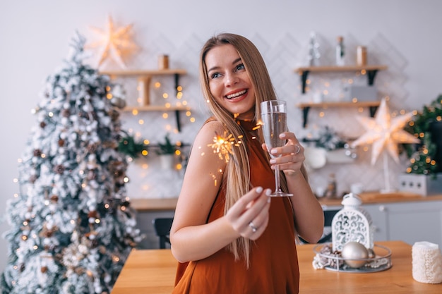 Atrakcyjna kobieta w pokoju bożonarodzeniowym z szampanem w dłoniach i brylantową blondynką jest gotowa do świętowania