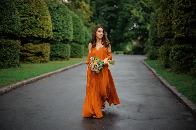 Atrakcyjna Kobieta W Pomarańczowej Sukience Chodzenie Po Drodze Z Bukietem Kwiatów