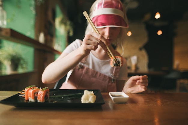 Atrakcyjna kobieta w różowej czapce zjada sushi rolki pałeczkami