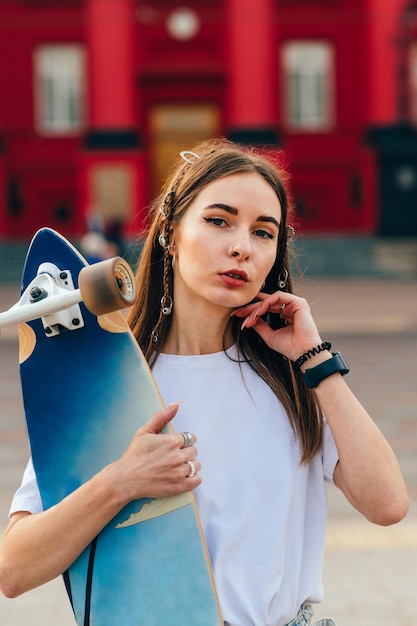 atrakcyjna łyżwiarka na ulicy z longboardem w dłoniach pozująca do kamery