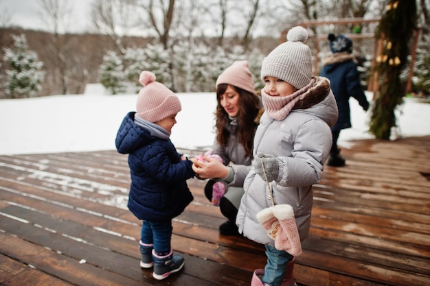 Zdjęcie atrakcyjna mama z dwiema ślicznymi córkami w zimowy dzień mama wkłada niemowlęcą rękawiczkę