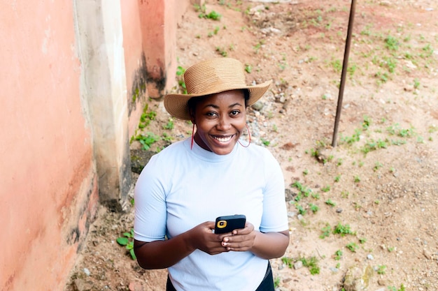 Atrakcyjna młoda afrykańska czarna dziewczyna trzyma telefon komórkowy i uśmiecha się patrząc na kamerę