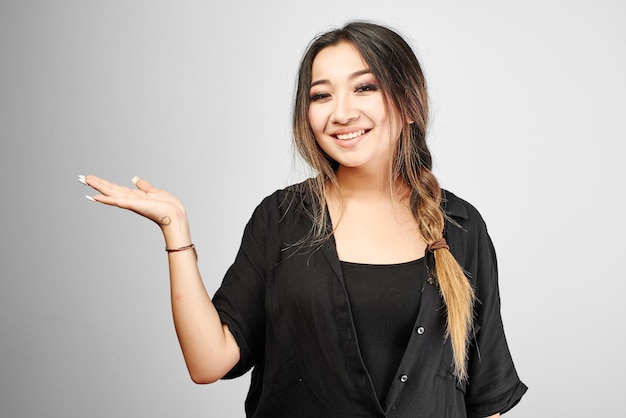 Atrakcyjna młoda Azjatka z Kazachstanu, w całkowitej czerni, uśmiechnięta i udająca, że trzyma Twój produkt lub tekst w dłoni na białym tle