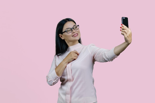 Atrakcyjna młoda azjatycka kobieta w okularach bierze selfie na swoim smartfonie