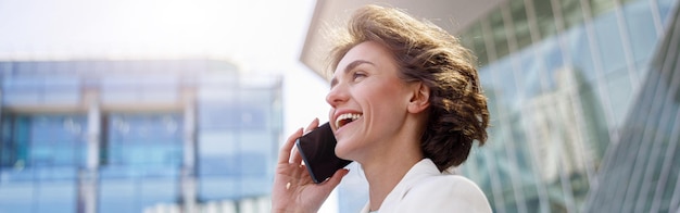 Atrakcyjna młoda bizneswoman rozmawia przez telefon stojący w pobliżu centrum biznesowego w białym garniturze