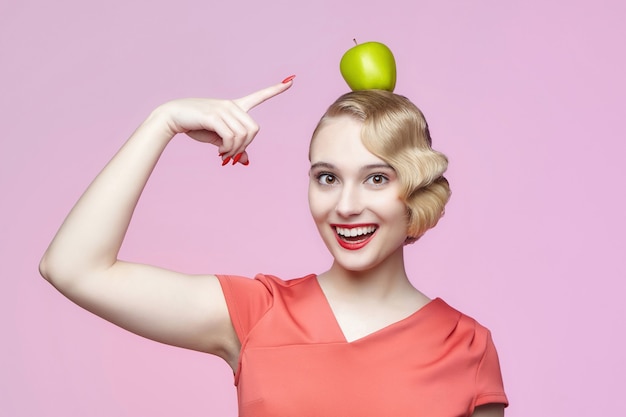 Atrakcyjna młoda blondynka z retro fryzurą i zielonym jabłkiem na głowie