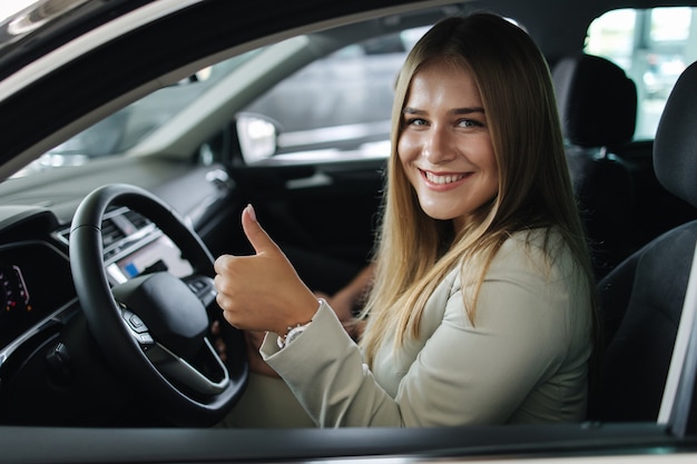 Atrakcyjna młoda bussines kobieta siedzi w samochodzie w salonie samochodowym kobieta wybiera nowy samochód piękna blondyna