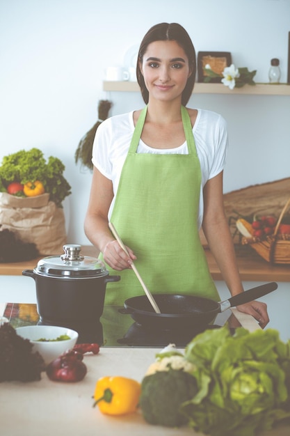 Atrakcyjna młoda ciemnowłosa kobieta smażąca posiłek na robaczkowej patelni według nowego przepisu na keto, stojąc i uśmiechając się w kuchni Koncepcje gotowania i prowadzenia gospodarstwa domowego