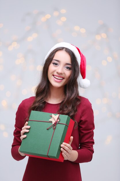Atrakcyjna młoda dama w Boże Narodzenie kapelusz trzyma pudełko na niewyraźne tło