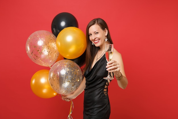Atrakcyjna młoda dziewczyna w małej czarnej sukience obchodzi trzymać kieliszek szampana balonów na białym tle na czerwonym tle. Międzynarodowy dzień kobiet szczęśliwego nowego roku urodziny makieta wakacje koncepcja strony.