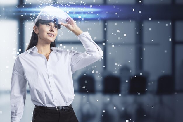 Atrakcyjna młoda europejska kobieta z abstrakcyjnym hologramem i okularami VR w rozmytym wnętrzu biura Rzeczywistość rozszerzona i koncepcja cyberprzestrzeni