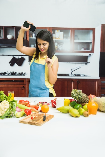 Atrakcyjna Młoda Indyjska Dziewczyna W Fartuchu Gotuje W Kuchni Ze Stołem Pełnym Owoców I Warzyw