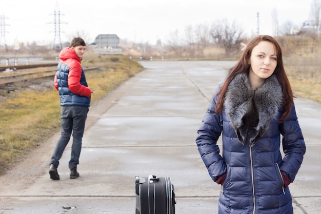 Atrakcyjna Młoda Kobieta Czeka Na Windę Na Wiejskiej Drodze Z Zapakowaną Walizką, Której Młody Mężczyzna Patrzy Na Nią, Gdy Przechodzi Obok