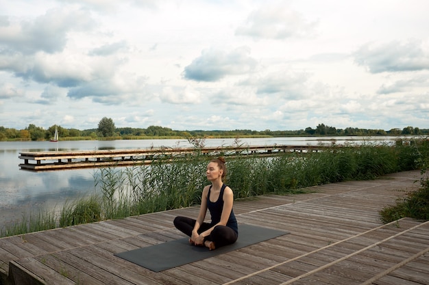 Atrakcyjna młoda kobieta lub model medytacji i praktykowania jogi na molo w pobliżu jeziora.
