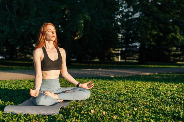 Atrakcyjna młoda kobieta medytuje siedząc w pozycji lotosu, siedząc na macie do jogi z zamkniętymi oczami