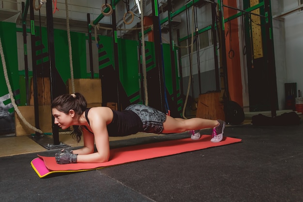 Atrakcyjna młoda kobieta robi deski ćwiczenie podczas gdy ćwiczący w gym