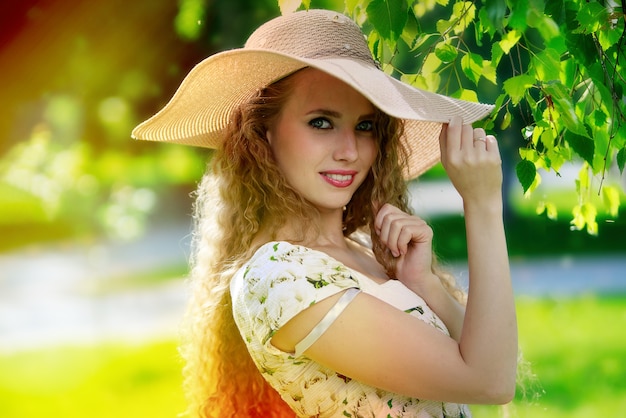 Atrakcyjna młoda kobieta w letniej sukience i kapeluszu, ciesząc się swoim czasem na świeżym powietrzu w parku
