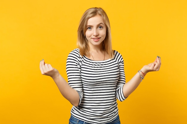 Zdjęcie atrakcyjna młoda kobieta w paski ubrania ocierając palce, pokazując gest gotówki, prosząc o pieniądze na białym tle na żółtym pomarańczowym tle. ludzie szczere emocje, koncepcja stylu życia. makieta miejsca na kopię.