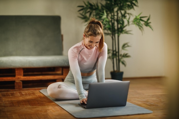 Atrakcyjna młoda kobieta za pomocą laptopa nagrywa swój vlog na temat zdrowego trybu życia podczas ćwiczeń w domu.