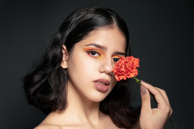 Atrakcyjna młoda kobieta ze złotym cieniem na oczy z kwiatem goździka na czarnym tle