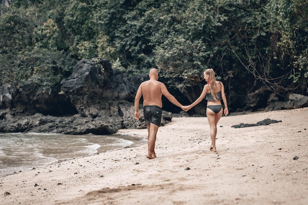 Atrakcyjna młoda para modny w białych strojach idą po plaży i trzymając się za ręce. Piękna blondynka z długimi włosami i łysy mężczyzna są na wakacjach. Phuket. Tajlandia.